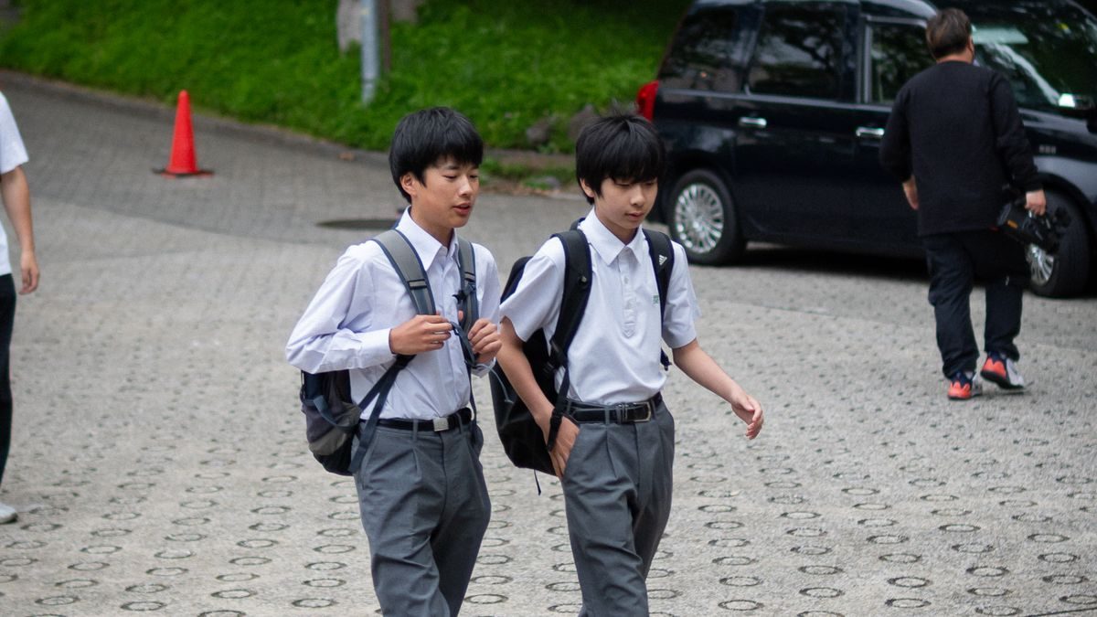 かばんを持った生徒二人が住宅街の坂道を歩いて登校している