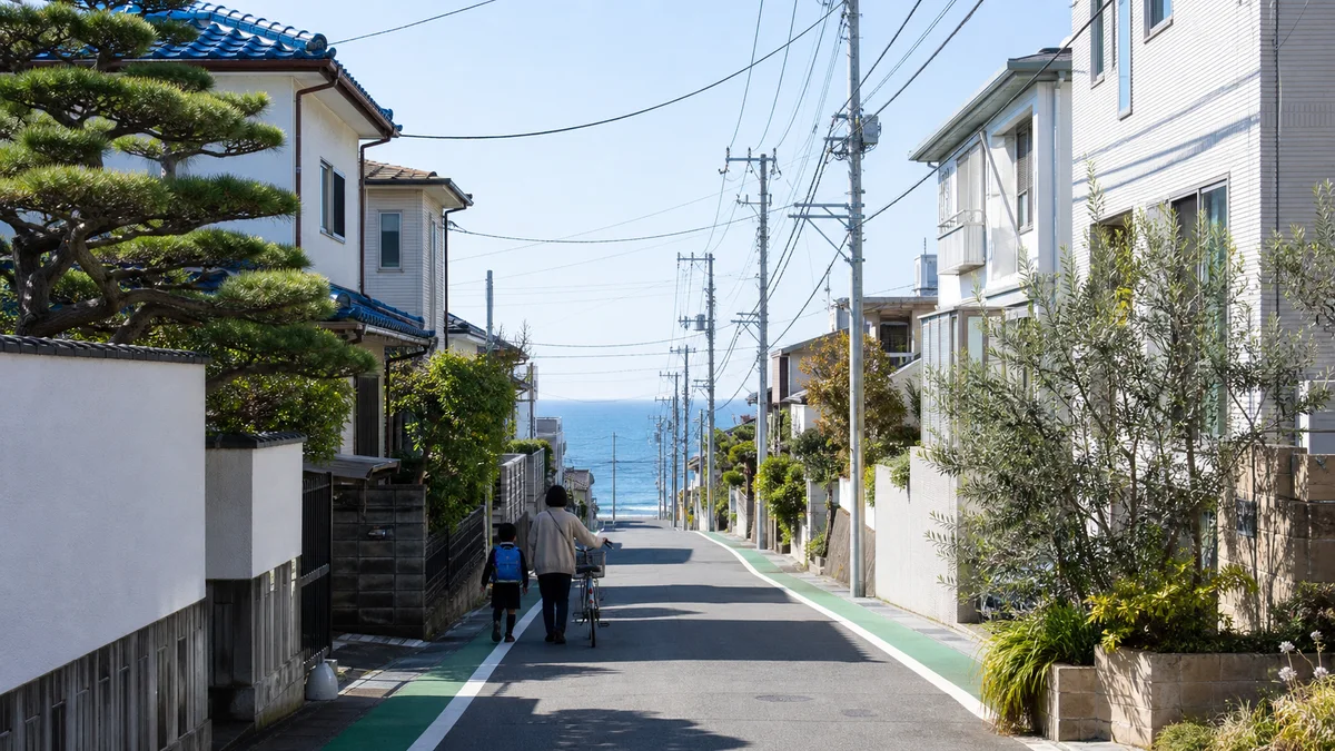 海へ続く藤沢市の住宅街を、親子が自転車を押しながら歩く暮らしのイメージ