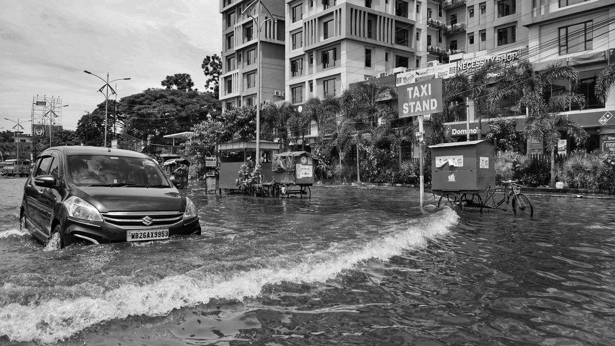 冠水した市街地の道路を、水しぶきを上げながら乗用車が走っている様子