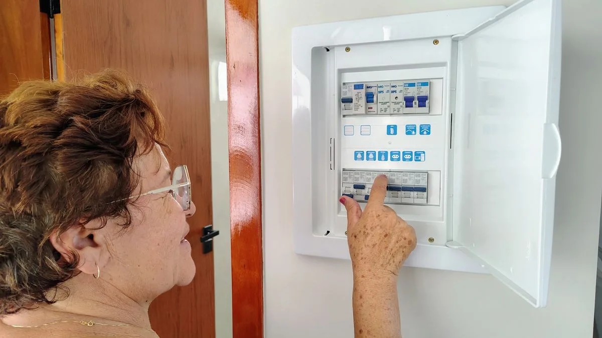 家の壁にある分電盤のふたを開けて、ブレーカーのつまみに手を伸ばしている人