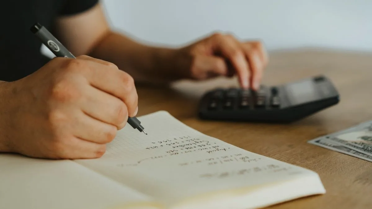 ノートに手書きで数字を書きながら、もう一方の手で電卓をたたいている手元
