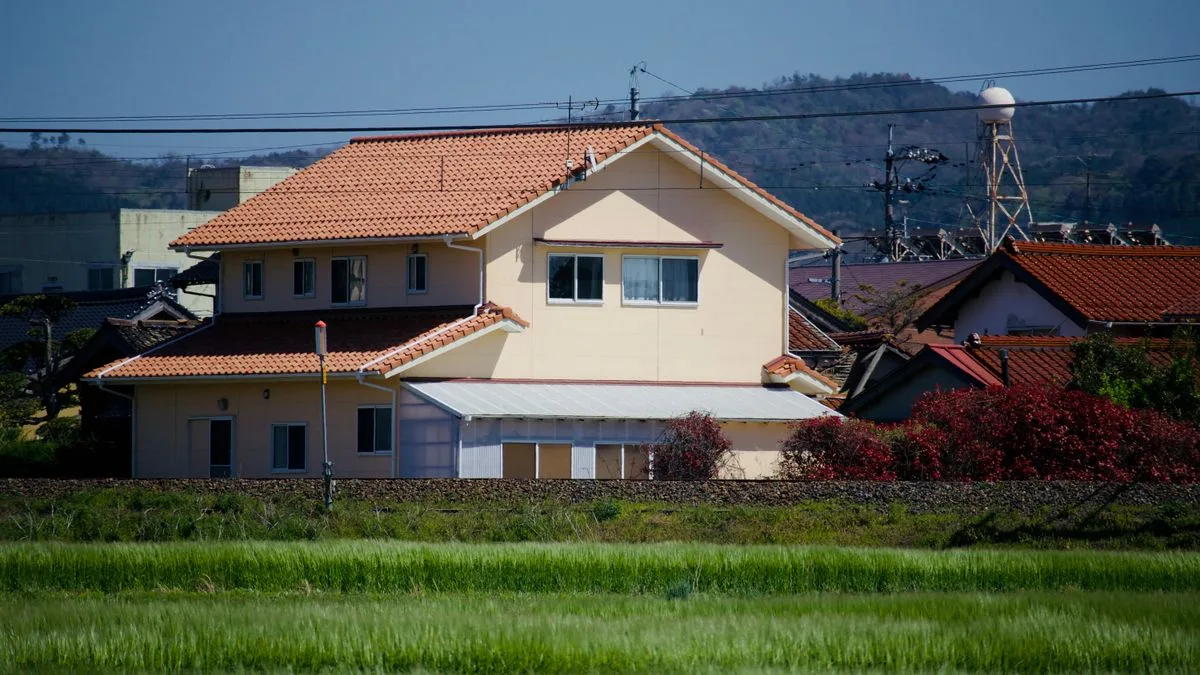 田んぼの向こうに瓦屋根の戸建てが並ぶ日本の郊外の集落
