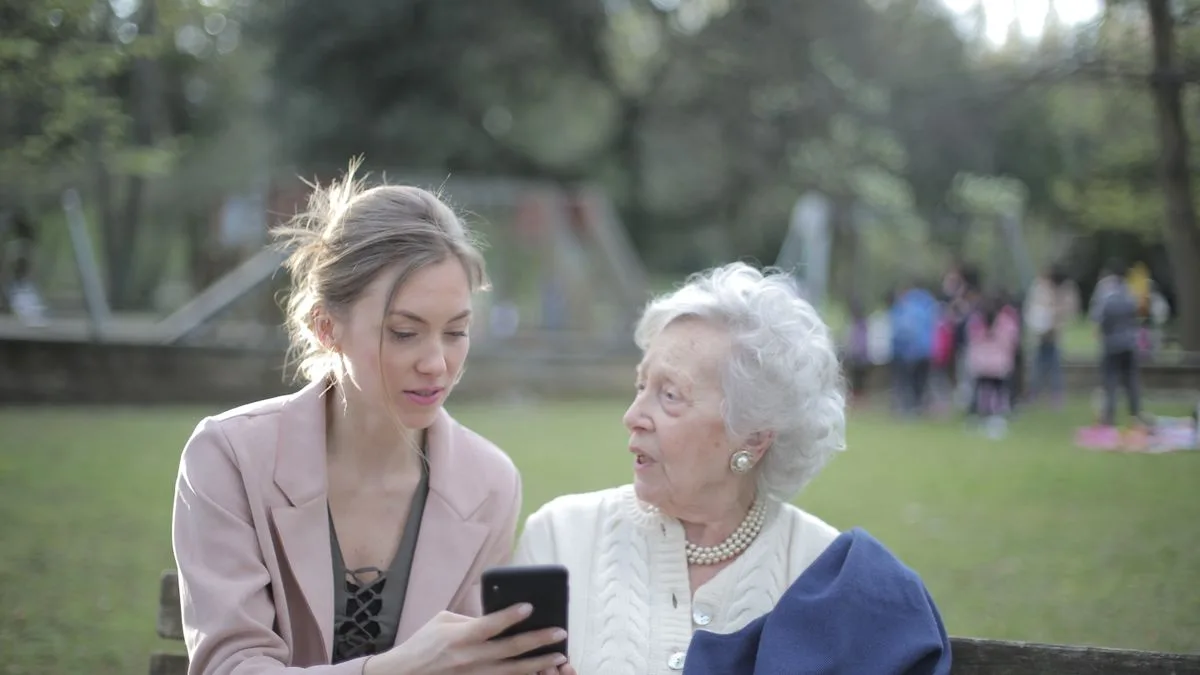 公園のベンチで、若い女性が高齢の女性にスマートフォンの画面を見せて説明している