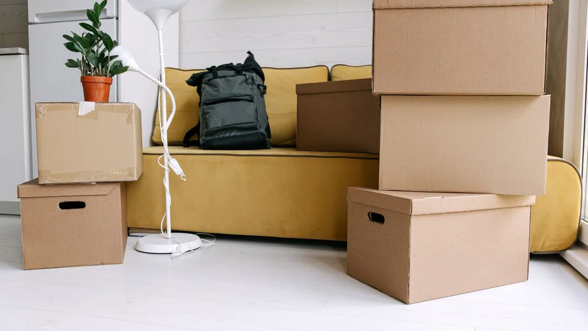 引っ越しの荷造りを終えた部屋。段ボール箱が積まれ、ソファの上にリュックが置かれている
