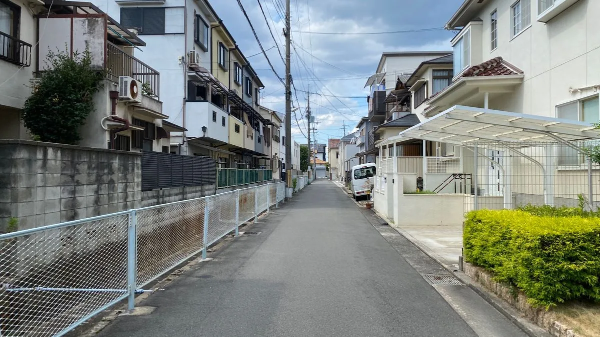 日ざしと影が落ちる日本の住宅街の道路。両側に2階建ての家が並ぶ