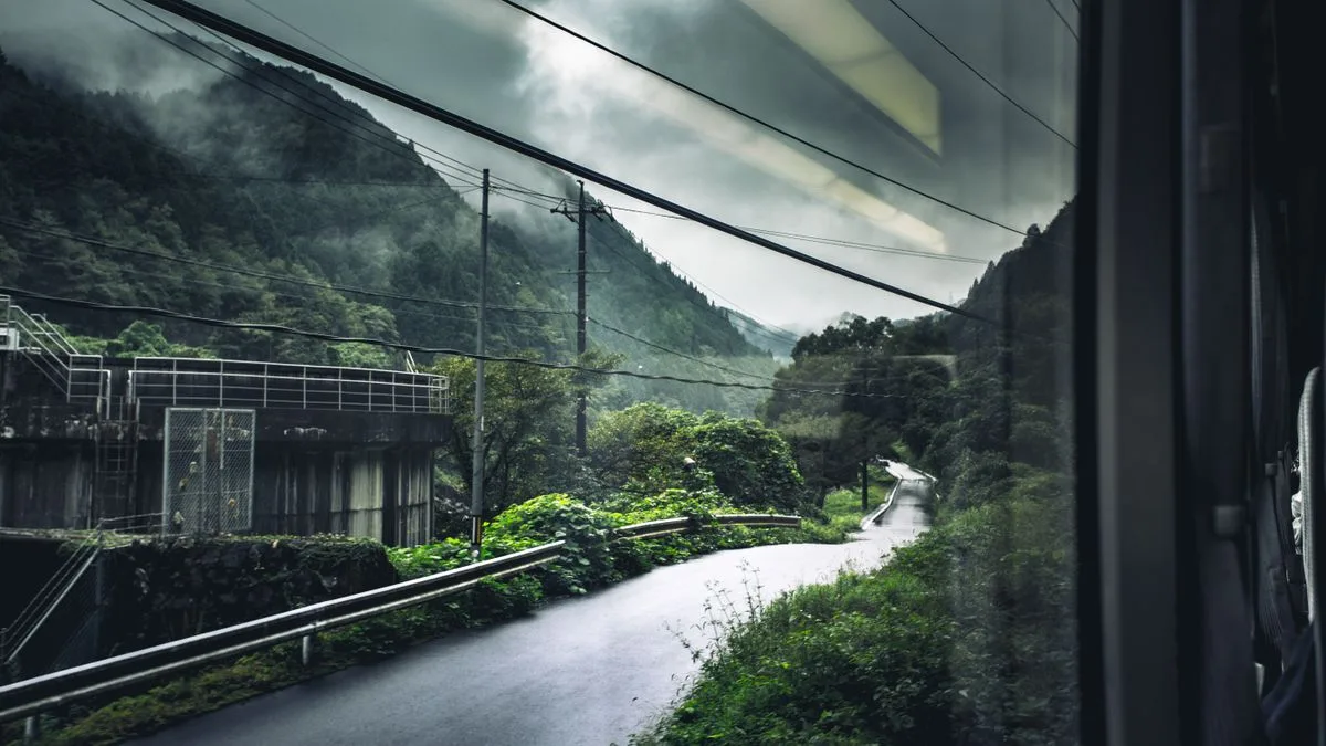 雨の日の車窓から見た山あいの風景。斜面に緑が広がっている
