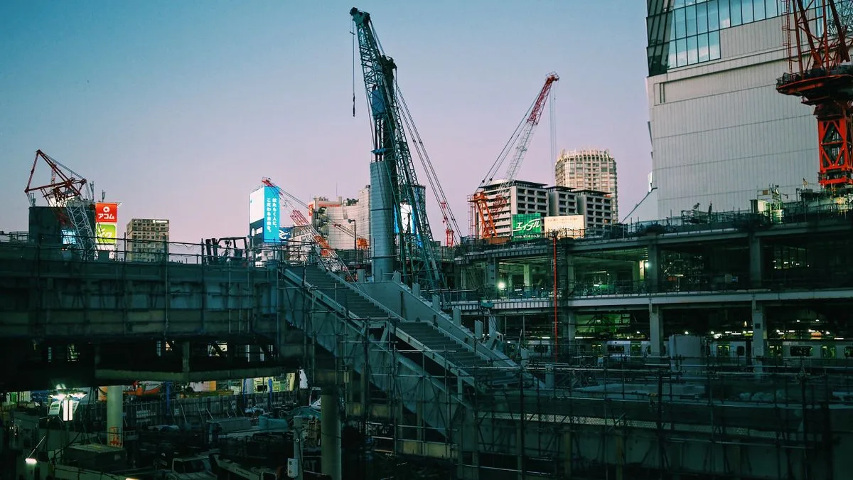 夕暮れの市街地に立ち並ぶ複数のクレーンと建設中の建物
