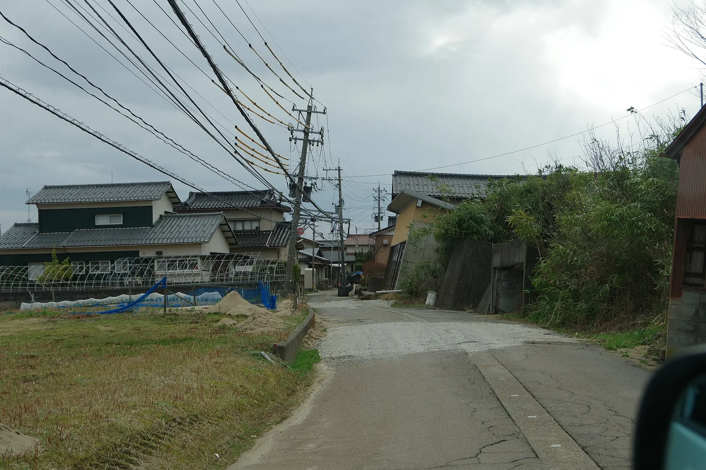 内灘町宮坂の道路。電柱が斜めに傾いて電線がたわみ、道路の脇の舗装が割れている
