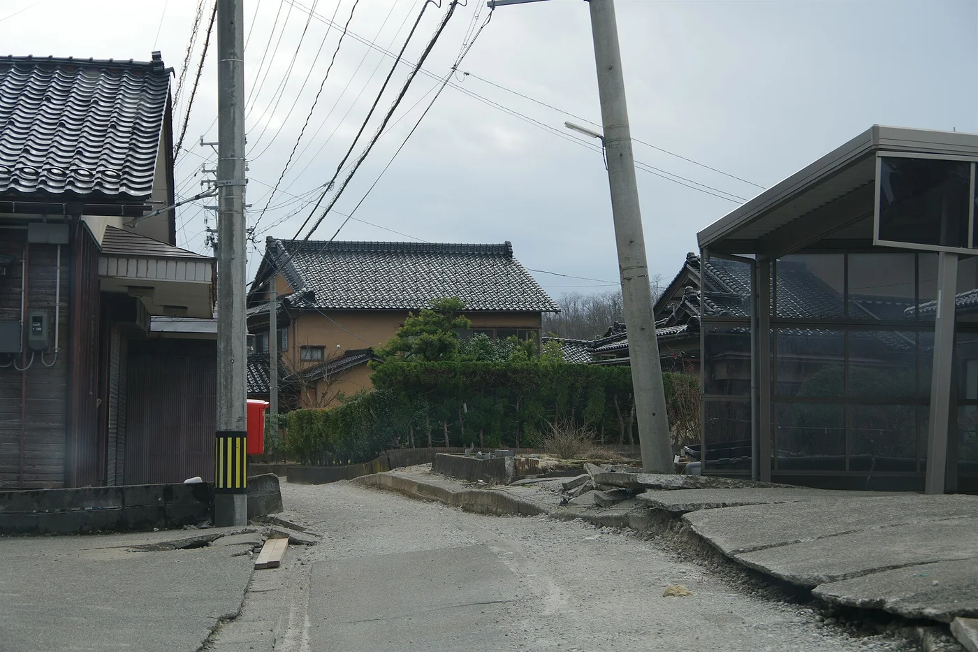 内灘町宮坂の道路。2本の電柱が傾き、コンクリートの路面が段差をつくって割れている