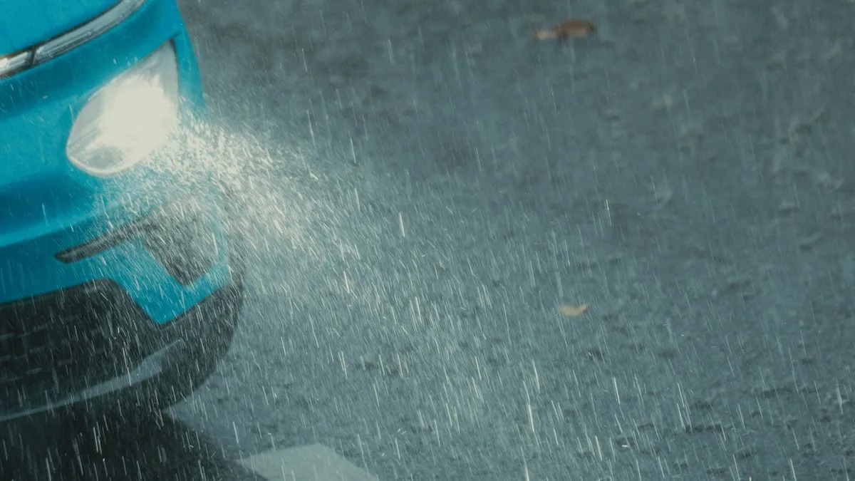 激しい雨のなか、ヘッドライトを点けた車が水の浮いた道路を走っている