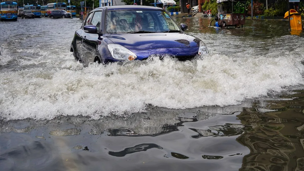 冠水した道路を、車体の下半分まで水に浸かりながら車が走っている
