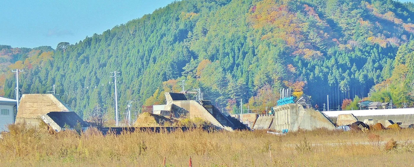 草地の向こうに残る田老の防潮堤跡。コンクリートの壁が途中で折れ、断面をさらしたまま並んでいる。背後は紅葉の始まった山