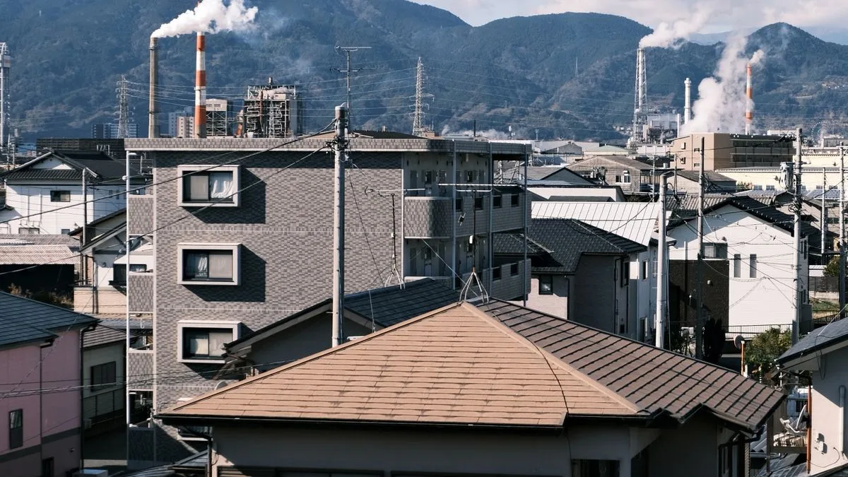 住宅の屋根が続く先に工場の煙突と設備が見える日本の街並み