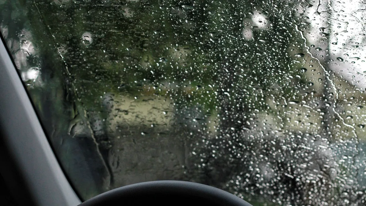 運転席から見た、雨粒がびっしりついたフロントガラスとハンドル