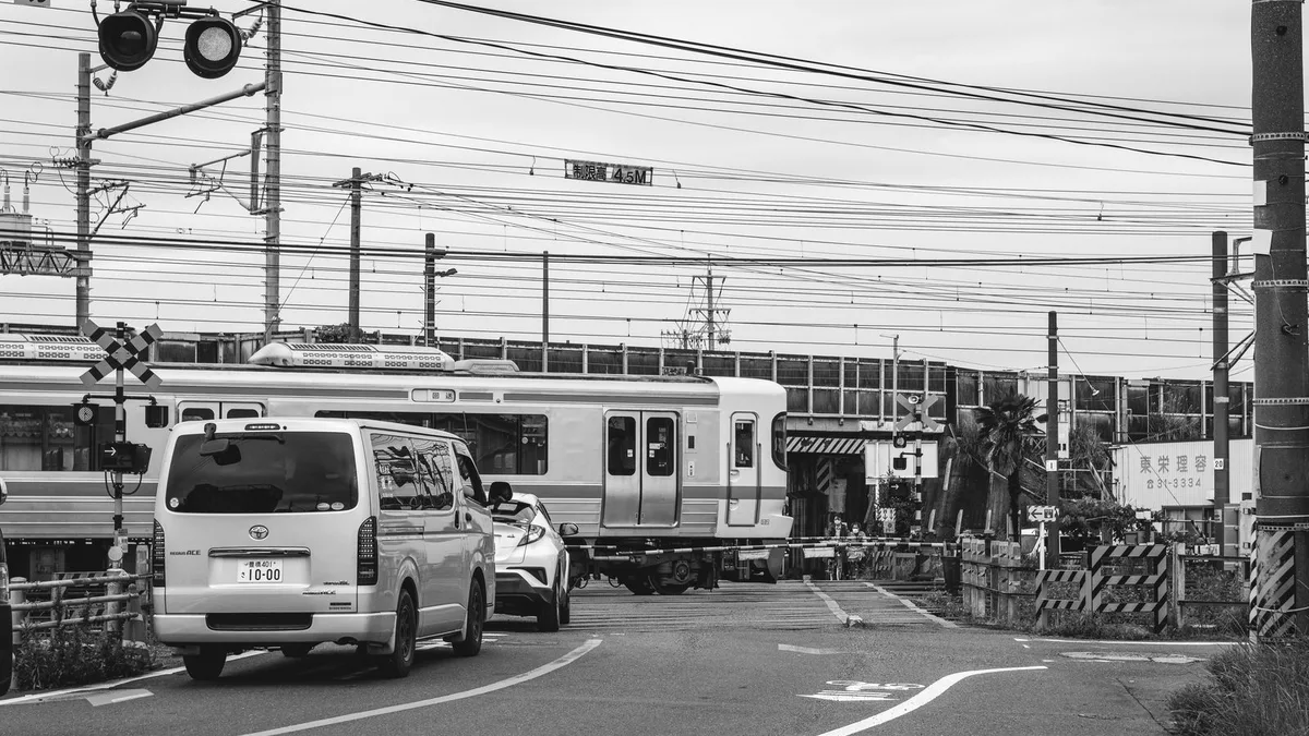 踏切で電車の通過を待つ車の列を白黒でとらえた写真