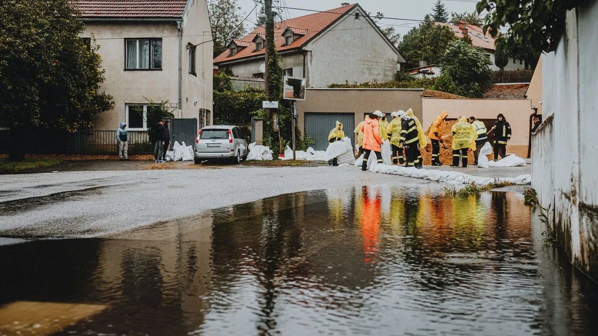 冠水した住宅街の道路。雨がっぱを着た人たちが土のうを並べている
