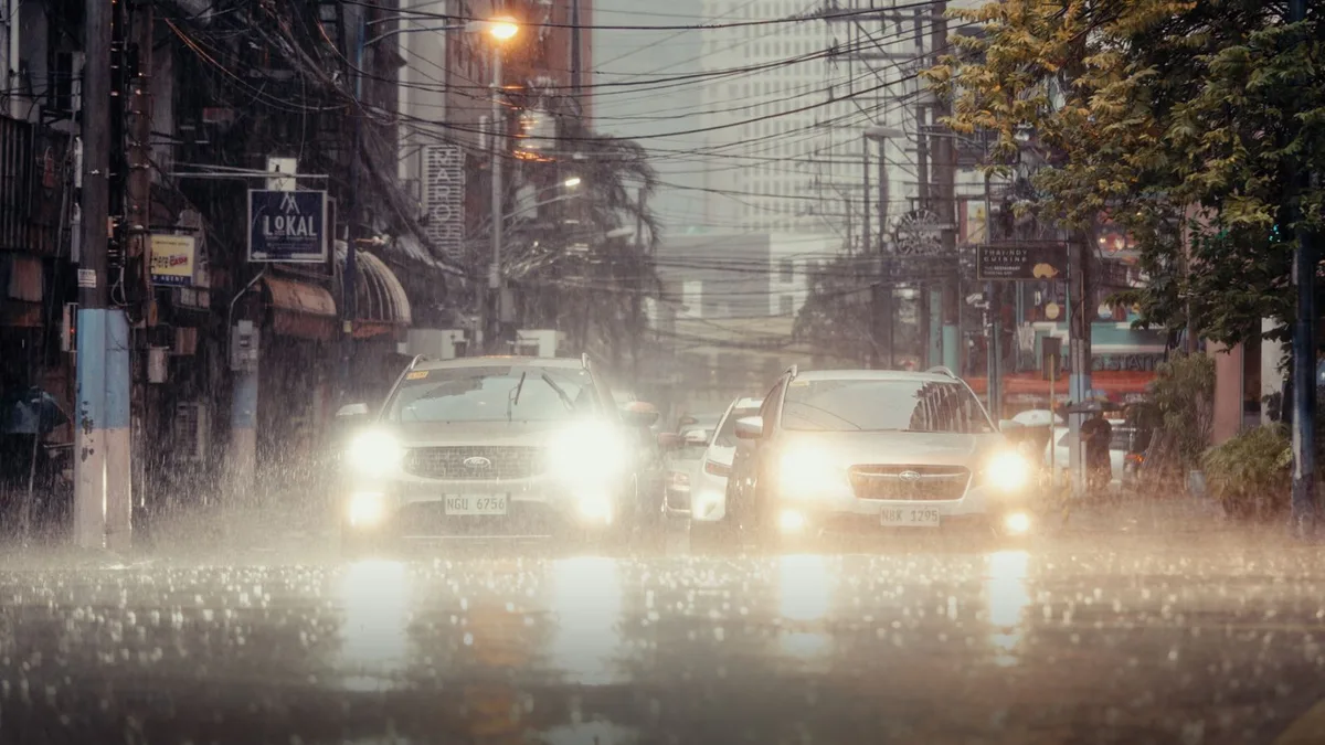 夜の豪雨のなかを、車が水しぶきを上げて走っていく街路