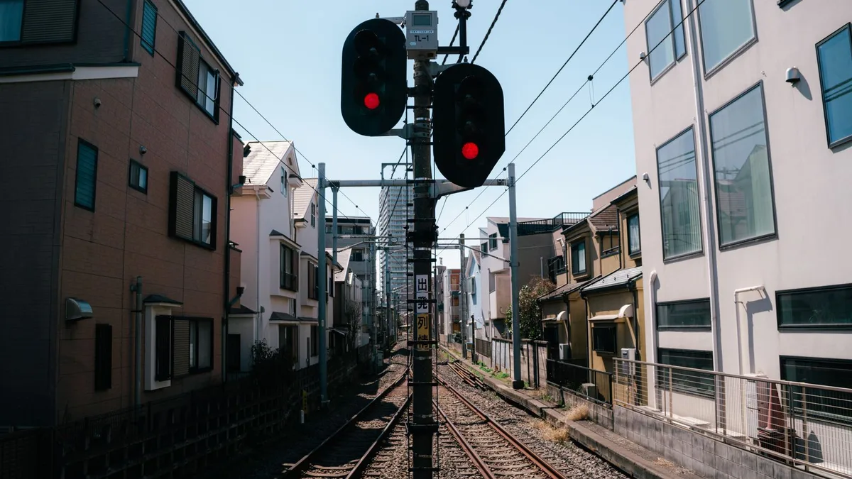 住宅にはさまれた線路と、赤く点灯した踏切の信号