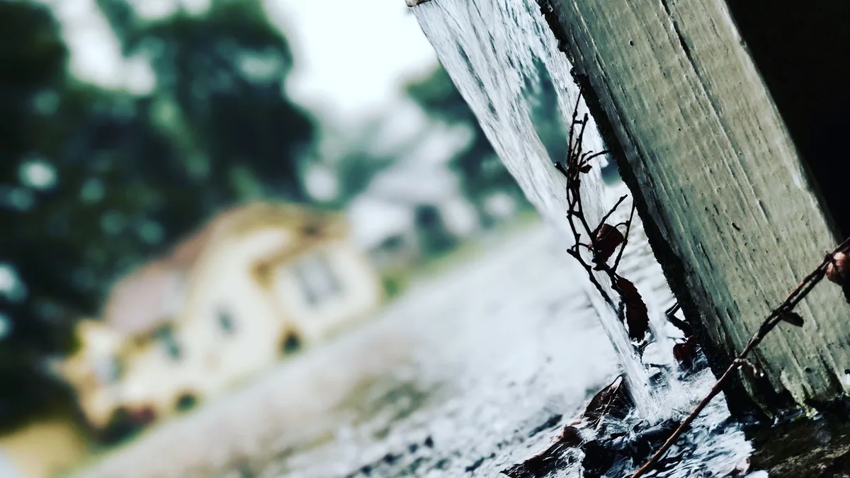 雨どいの端から雨水が勢いよく流れ落ち、足元の地面にたまっている