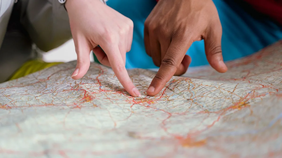 広げた紙の地図を2人が指でたどっている手元