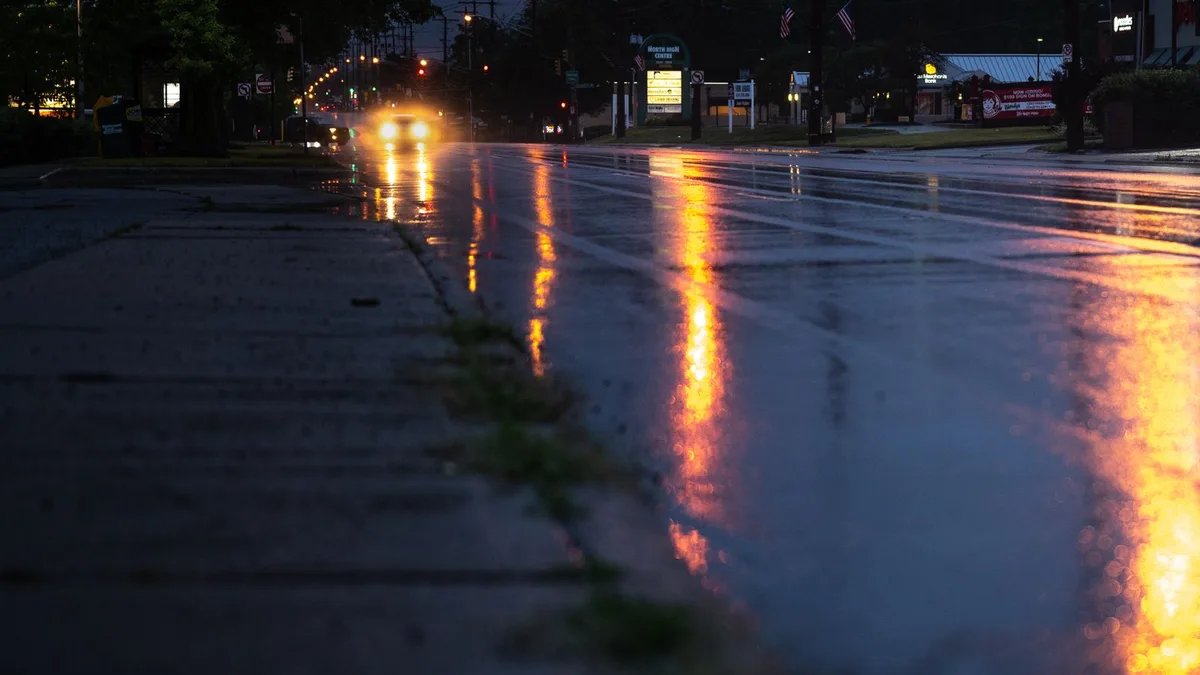 雨に濡れた夜の道路。路面に対向車のヘッドライトと店の明かりが長く反射している