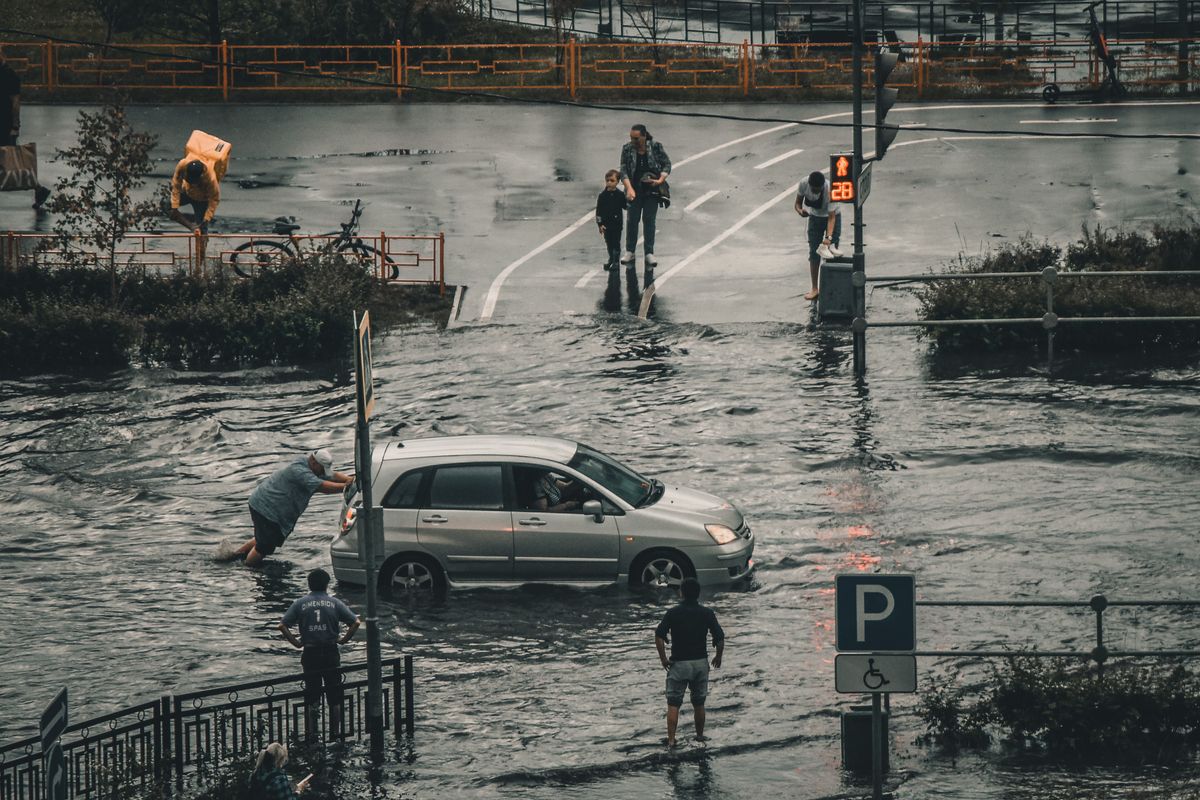 冠水した交差点で動けなくなった車と、水の中を歩く人たち