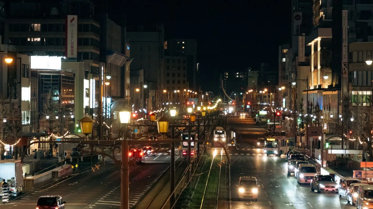 雨に濡れた夜の市街地の道路。車のライトが路面に反射している