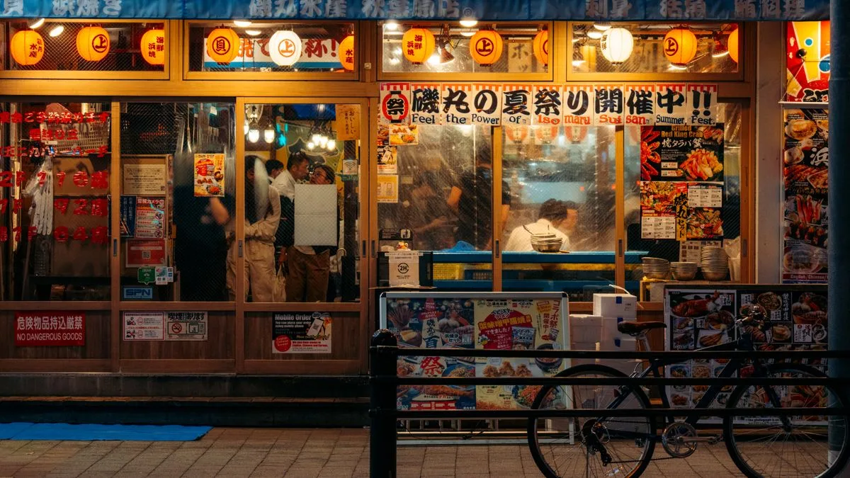 提灯とメニューの写真が並ぶ日本の飲食店の外観。夜に明かりがついている