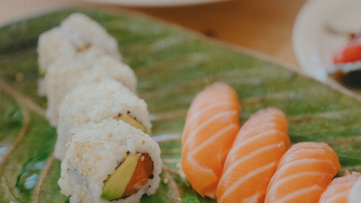 緑の葉を敷いた皿にサーモンの握りと巻き寿司が並んでいる