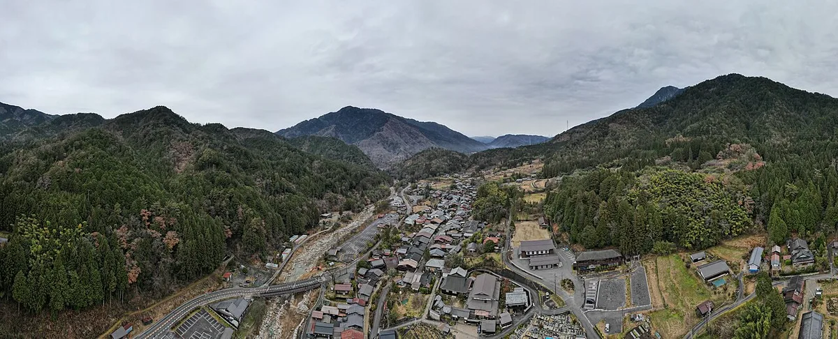 妻籠宿と周囲の山を上空から見た写真。谷の底に集落が細長く並ぶ