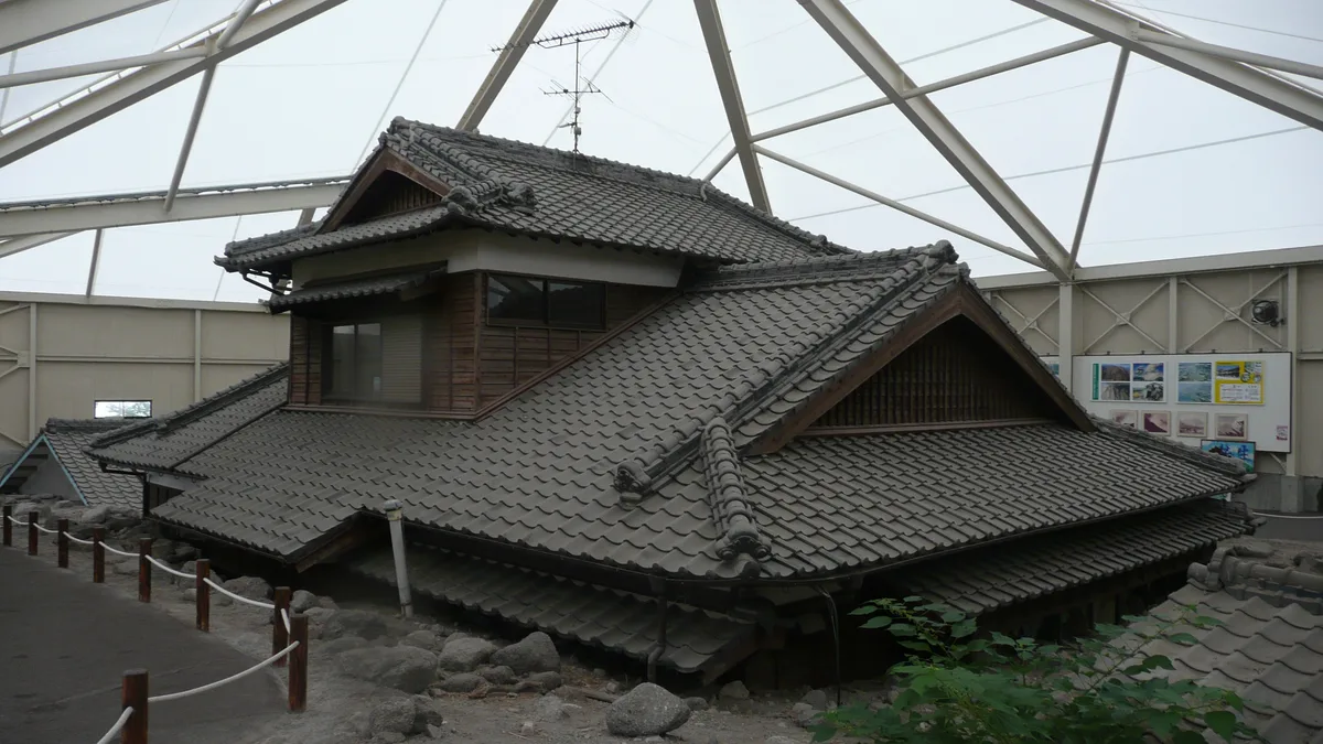 白いドーム状の屋根の下に、土石流で1階部分が土砂に埋まった木造家屋がそのまま保存されている