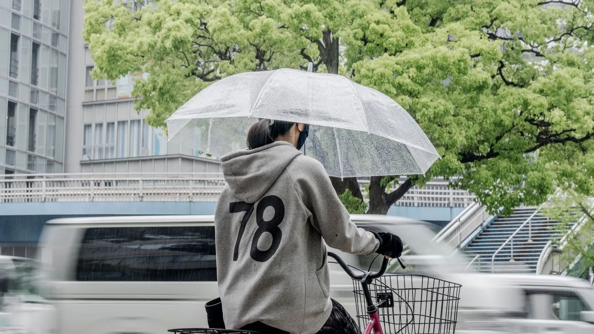 雨の街なかを、傘をさして自転車を押す人。路面が濡れている