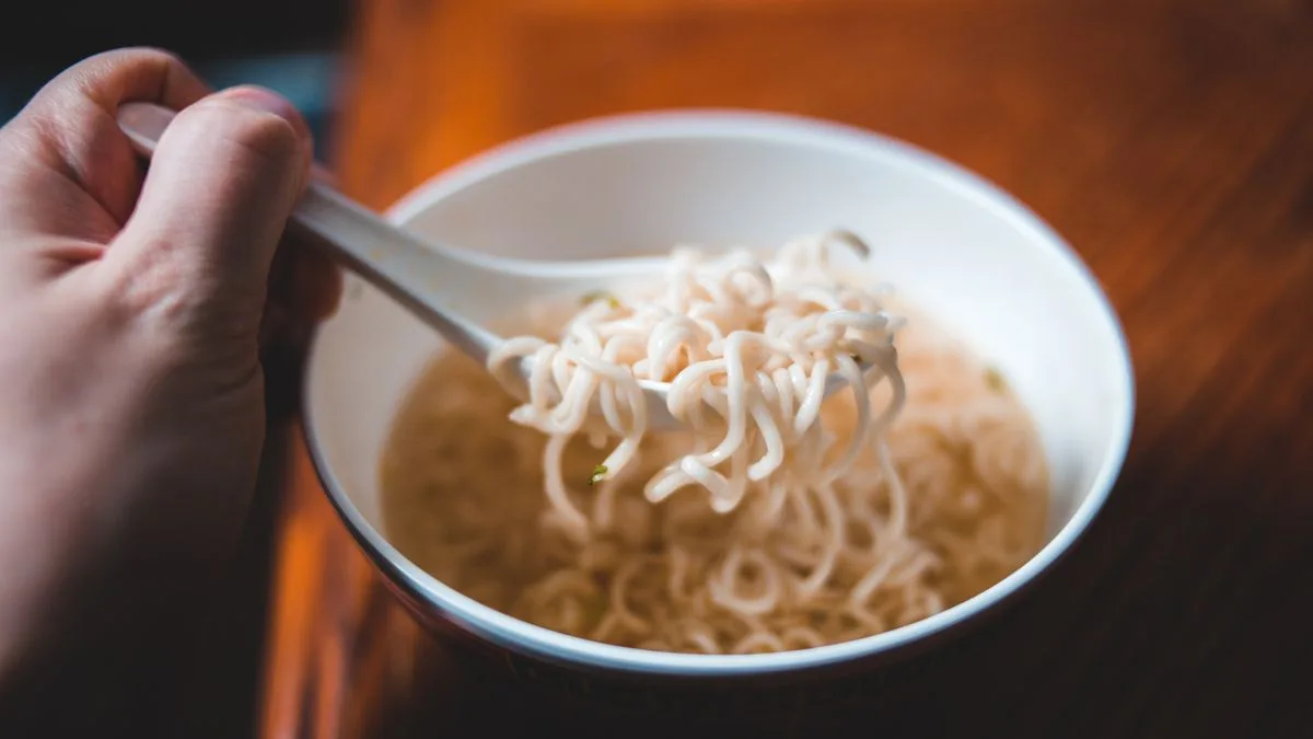 スープの張られた器から、レンゲでインスタント麺をすくい上げているところ
