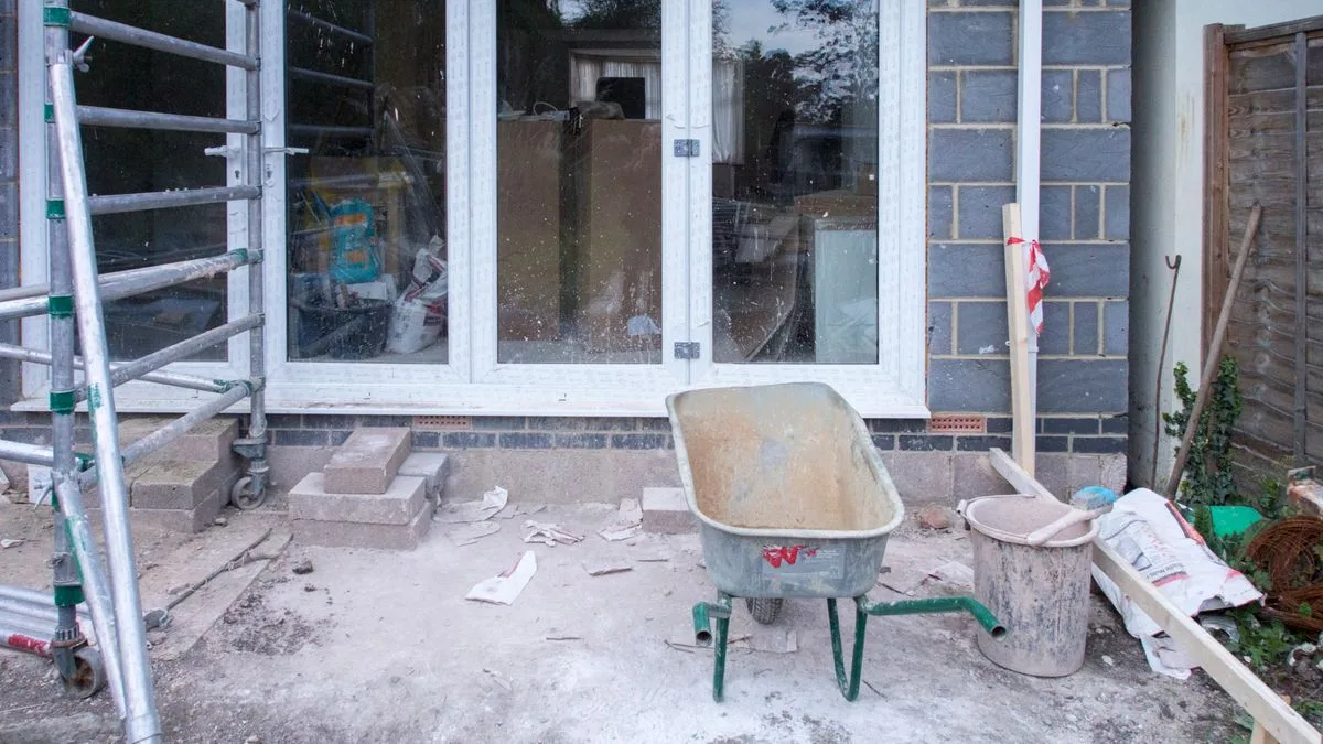 足場が組まれ、内装をはがして工事中の建物。前に一輪車と資材が置かれている