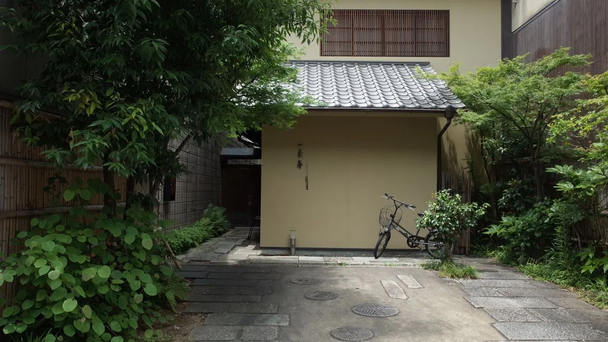 木の塀と生け垣に囲まれた日本の住宅の玄関まわり。建物の足元が地面と接している