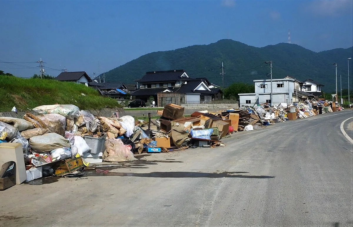 2018年7月14日、真備町の道路脇に積み上がった家財のごみと、背後の山