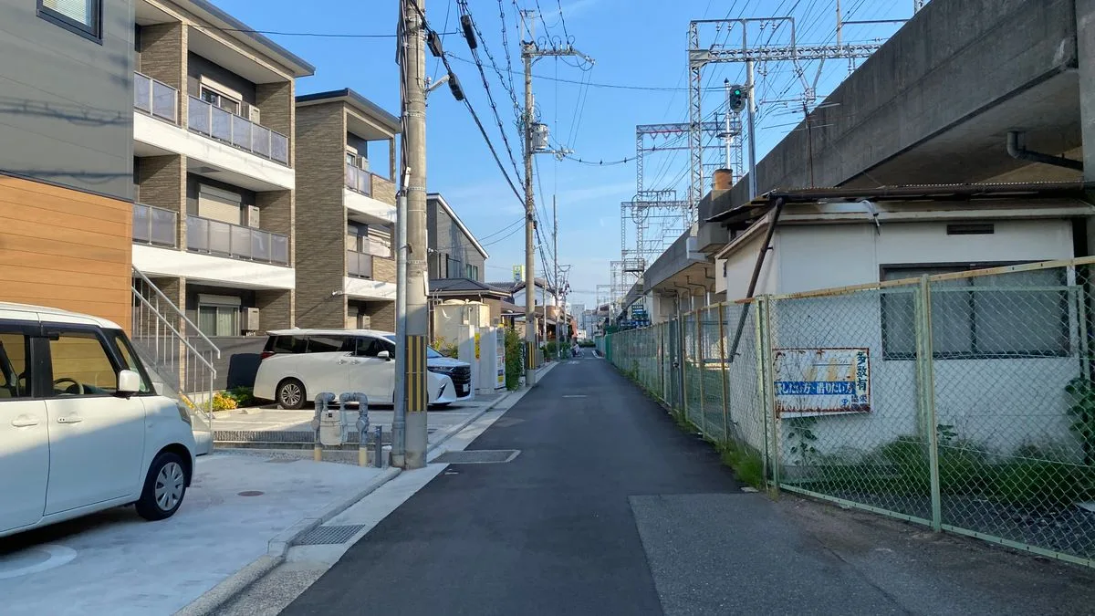 日本の住宅街。手前に賃貸アパートが建ち、その先に電線と道路が続いている