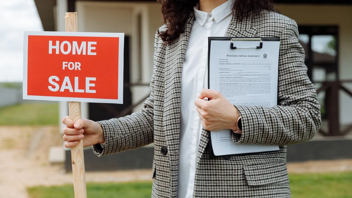 「HOME FOR SALE」の看板と書類を手に持つ不動産の担当者