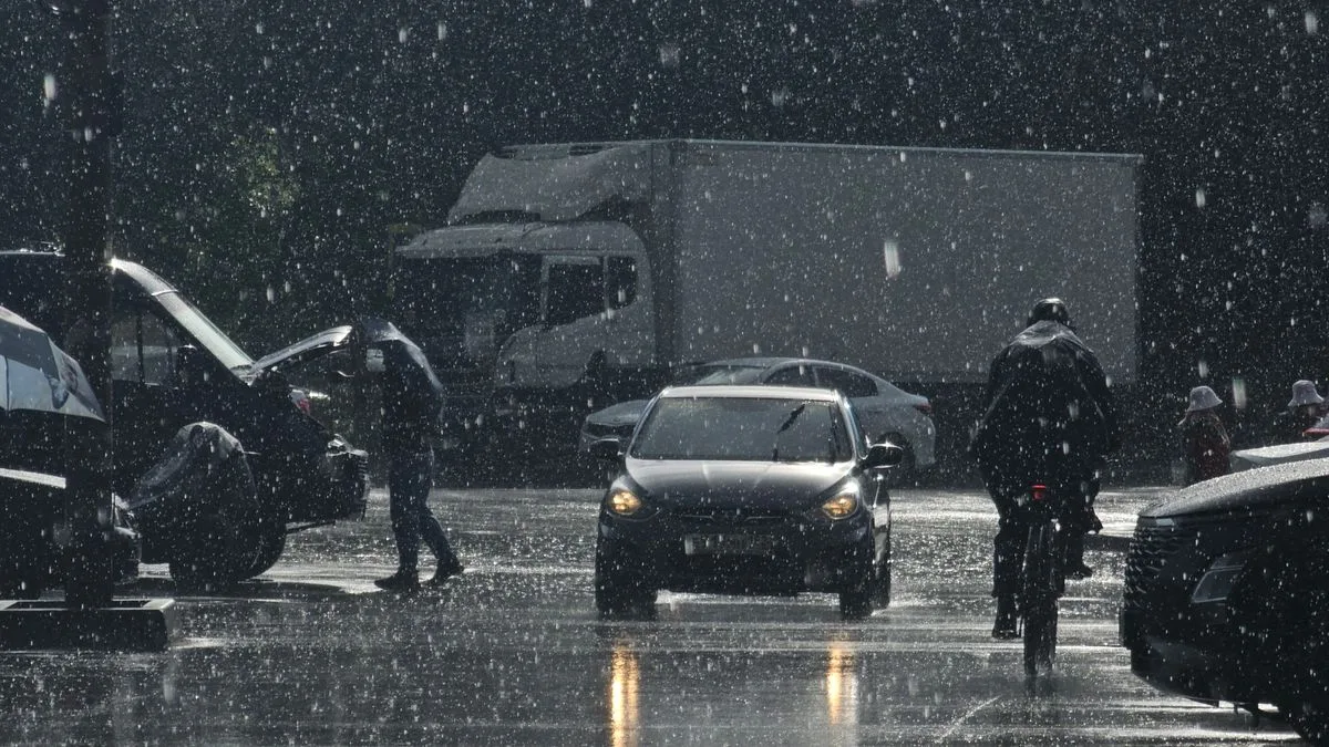 雨が強く降る街路。車のライトが濡れた路面に反射し、人が傘をさして歩いている
