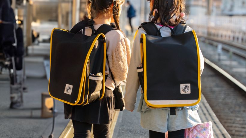 駅のホームでランドセルを背負って並ぶ子どもの後ろ姿。引っ越しと転校の場面を示す写真