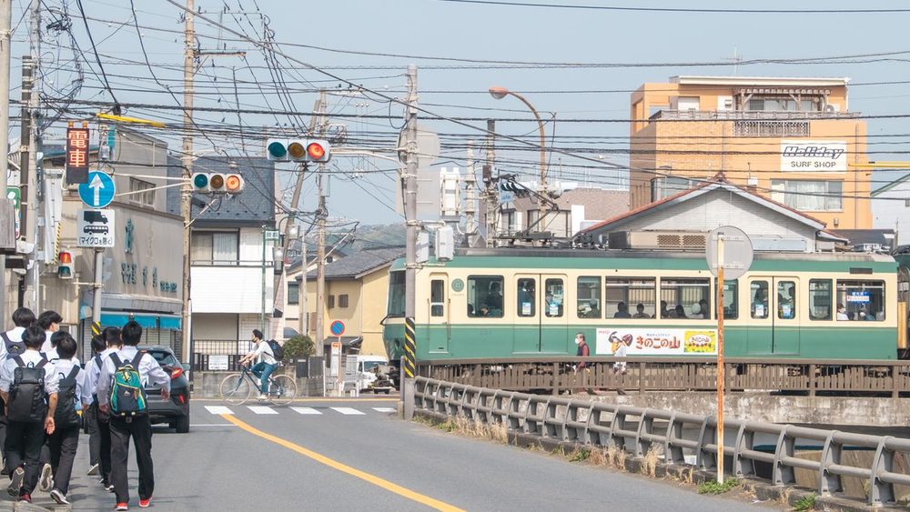 制服姿の中学生が、線路沿いの住宅街の道を歩いて登校している