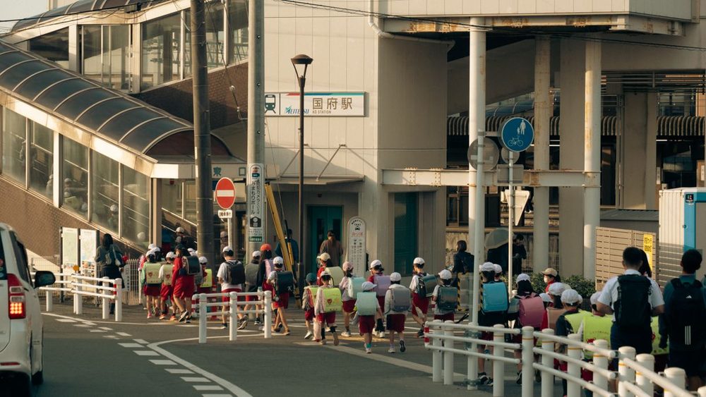 ランドセルを背負った小学生の集団が、駅前の横断歩道を列になって渡っている登校風景