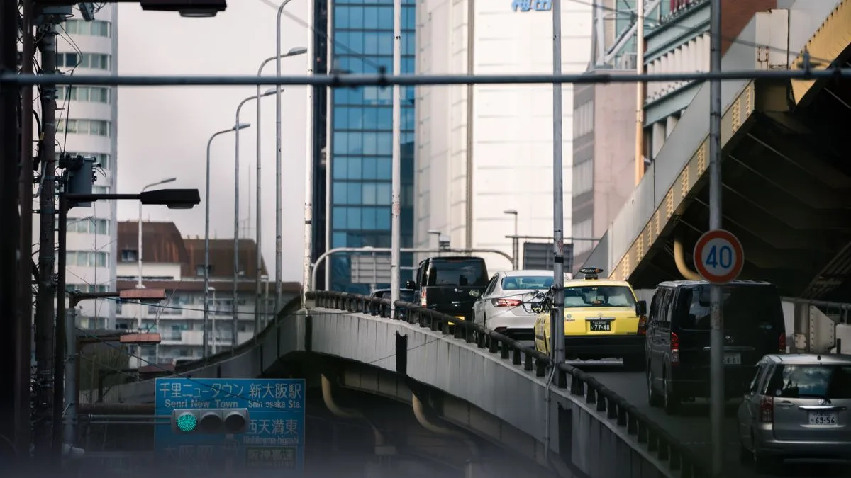 高架をくぐる市街地の道路を、車が列になって走っている