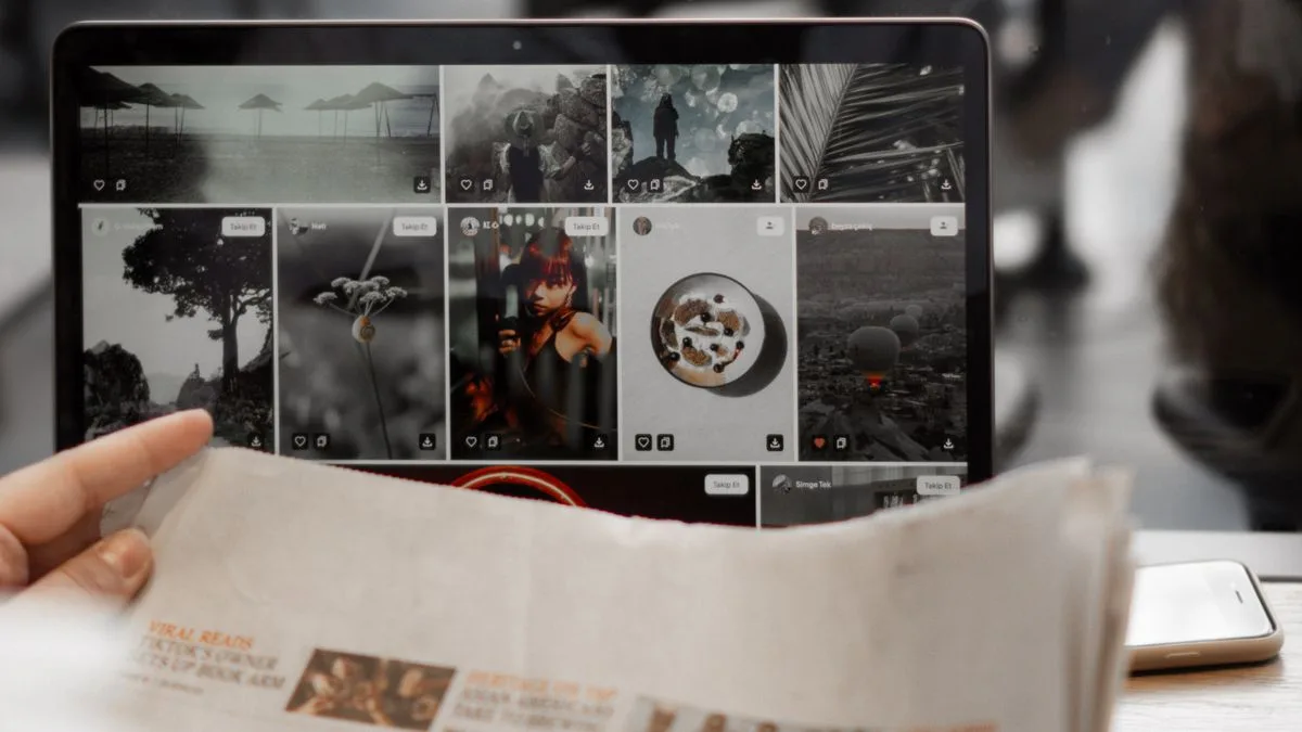 タブレット端末に写真の一覧が表示され、その手前に紙の新聞が広げられている机の上