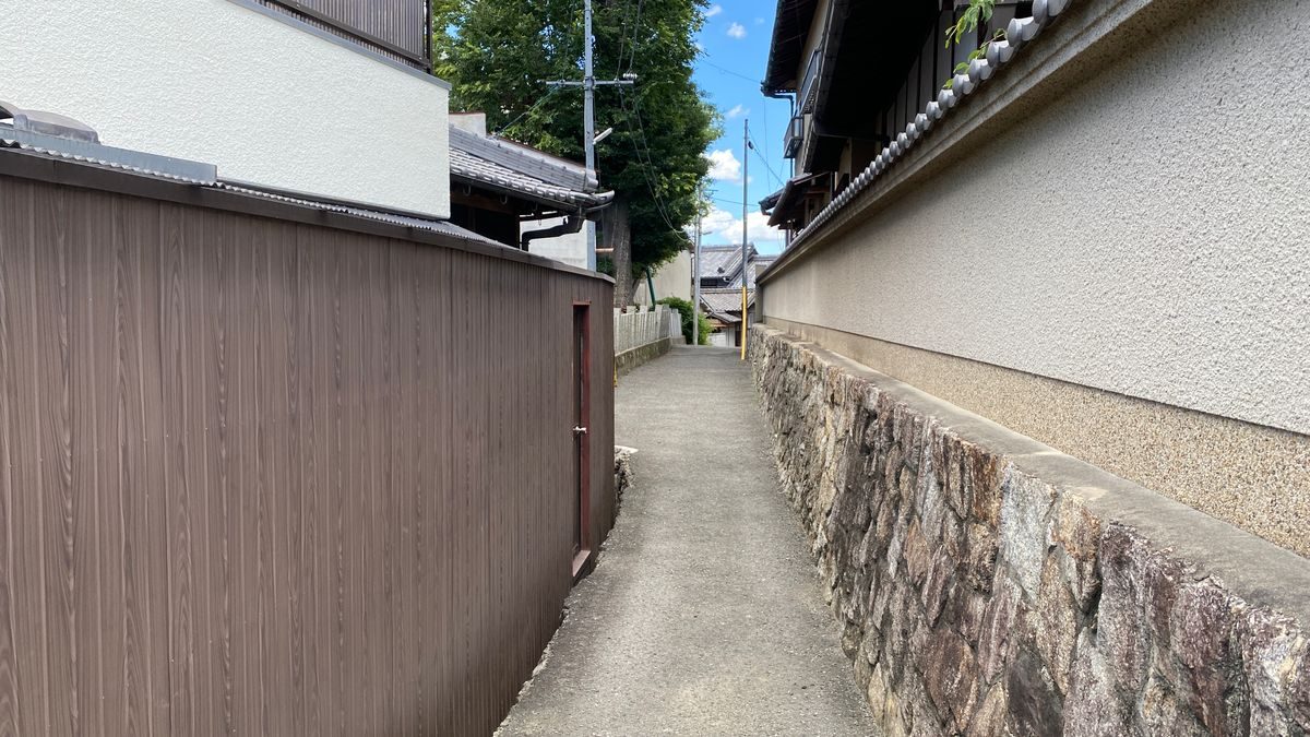 両側を塀にはさまれた細い通路。奥に住宅の屋根が見え、通路の幅が人ひとり分ほどしかない