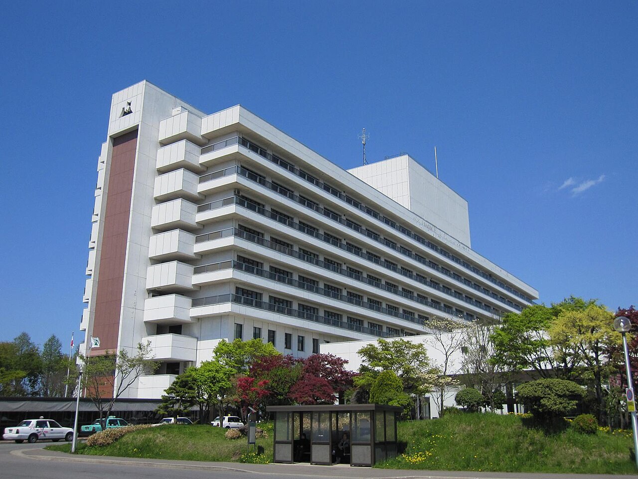 青森県立中央病院の白い大きな病棟と、手前の植え込みとバス停