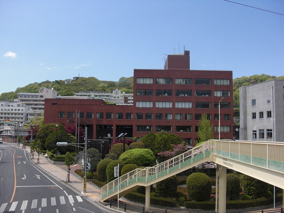 栃木県足利市役所の庁舎。赤れんが色の建物と植え込み、歩道橋