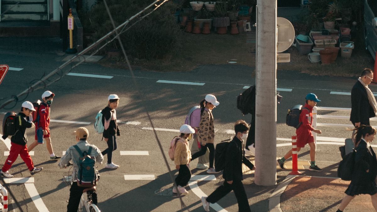 朝の横断歩道を、帽子をかぶりリュックを背負った子どもたちが次々に渡っていく。自転車の人や大人も行き交っている