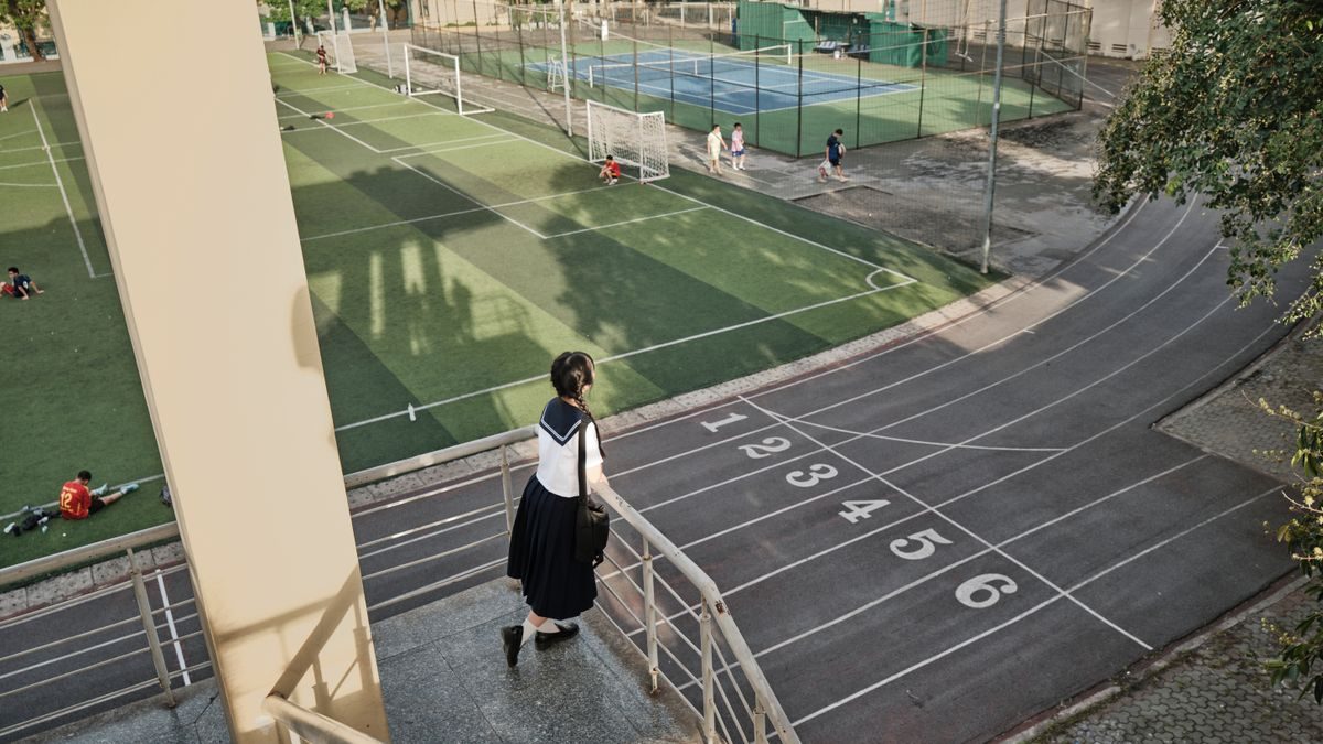 学校のグラウンドの脇の階段を、制服姿の生徒が下りていく。奥にサッカー場とテニスコート、手前に陸上トラック