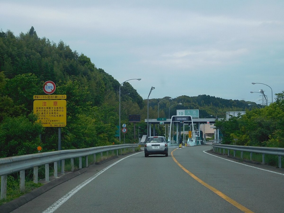 九州自動車道の人吉インターチェンジの料金所へ向かう道。手前の黄色い看板には、危険物を積んだ車は肥後トンネルと加久藤トンネルを通れないと書かれている